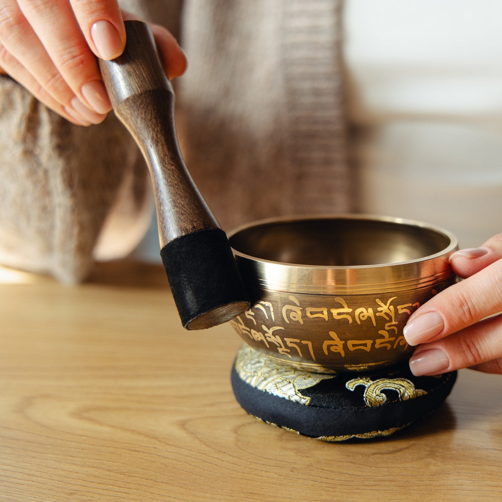 A hand gliding the wrapped end of the striker around the outside of a singing bowl