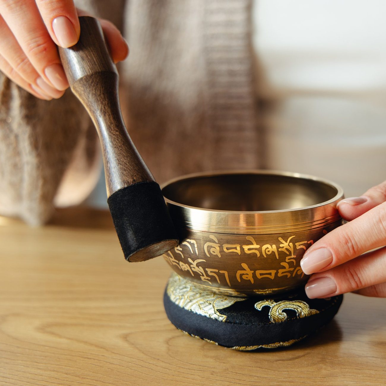 A hand tapping the outside of a singing bowl, just below the rim, with the leather-wrapped end of the striker