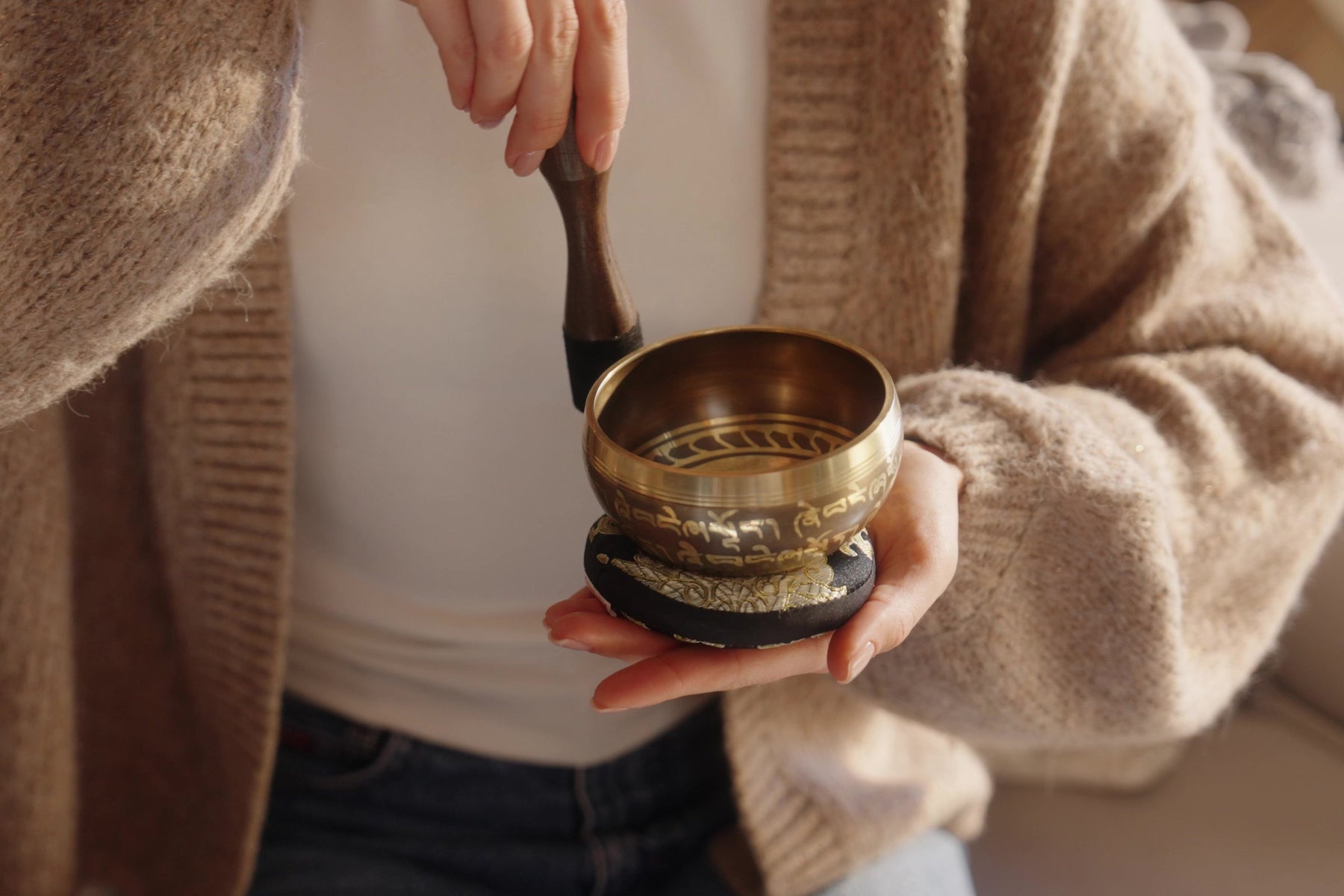 A hand playing a Silent Mind singing bowl, the striker held upright against the outside of the rim