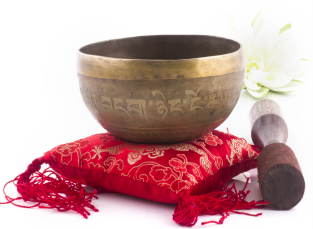 A small Silent Mind singing bowl sits atop a red cushion with its striker nearby.