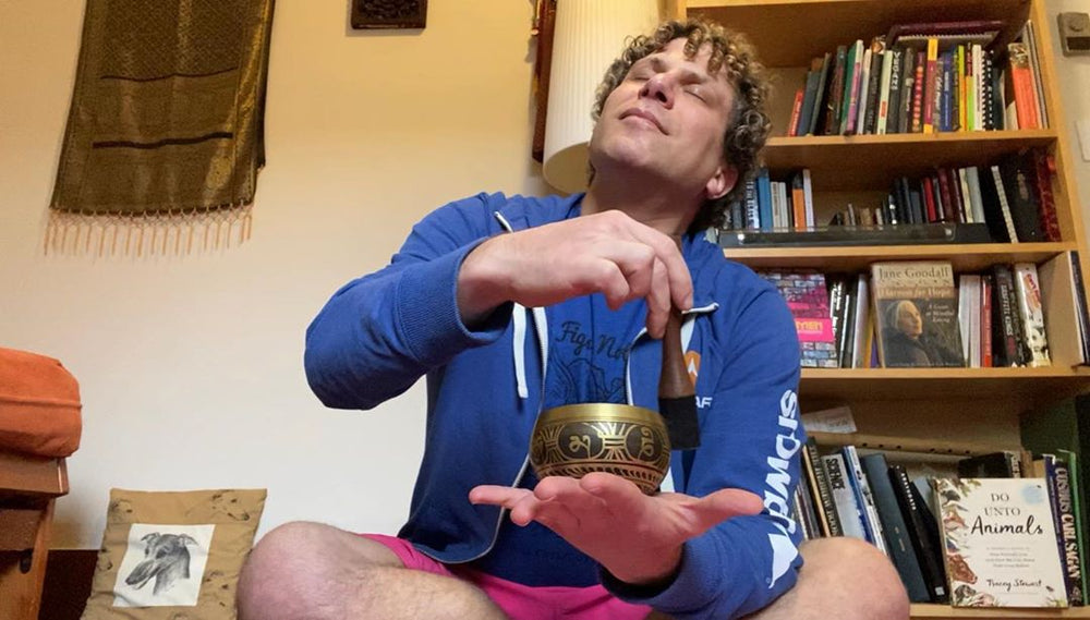 A man with curly hair sits peacefully at home, playing a Silent Mind singing bowl.