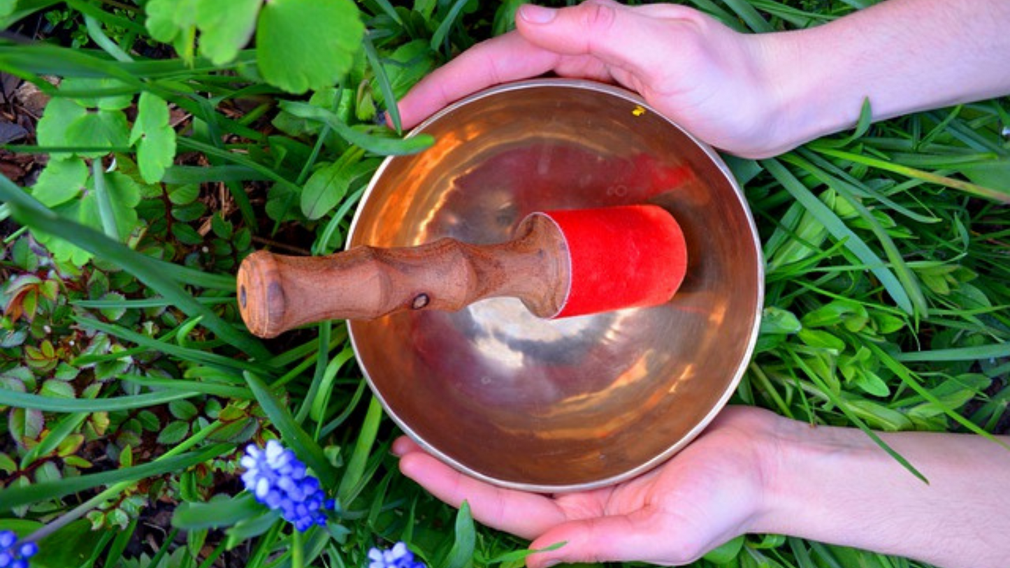 Holding a singing bowl in the grass field. Red striker.