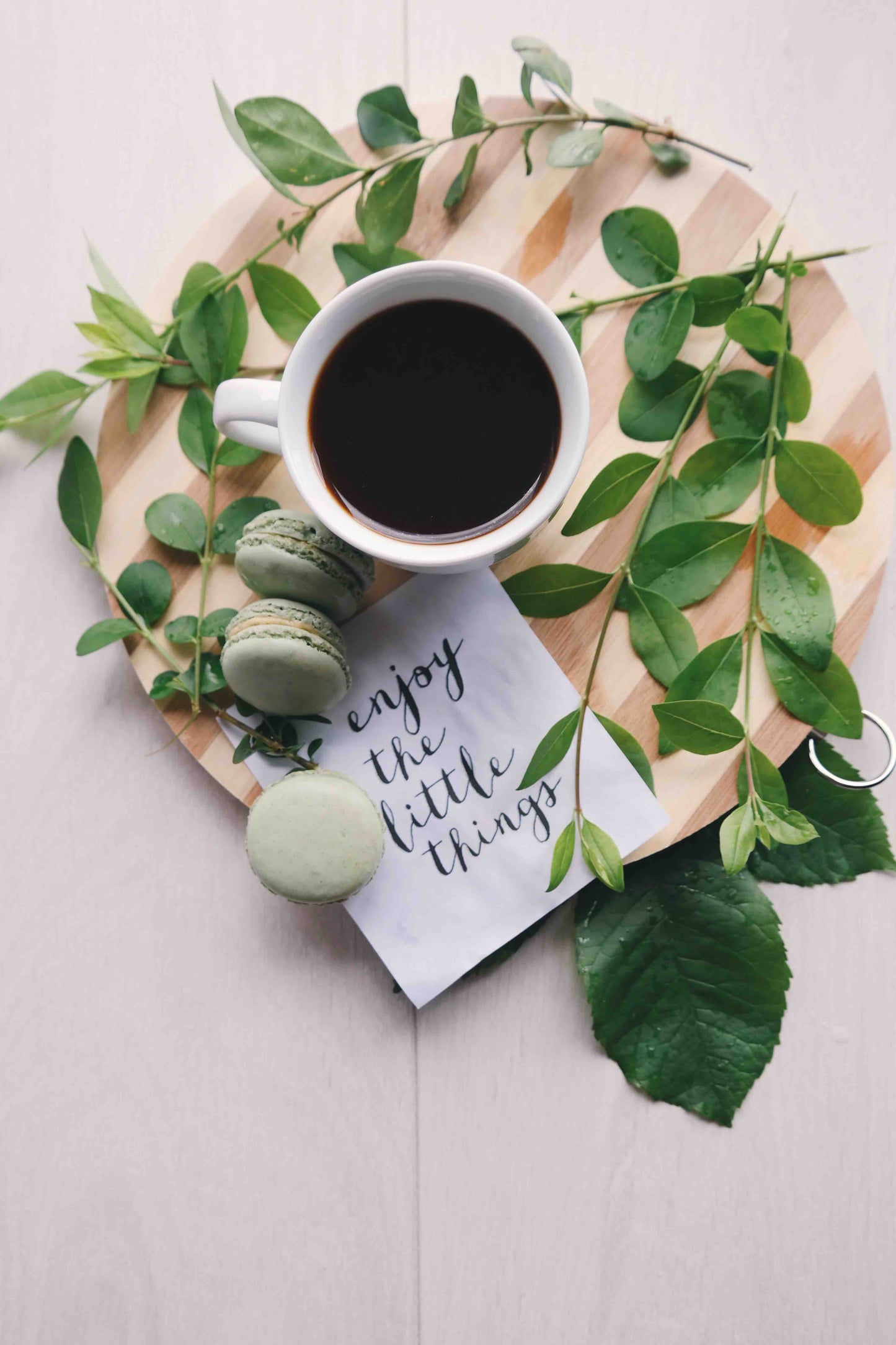 Coffee and macarons sit near a small sign reading "enjoy the little things"