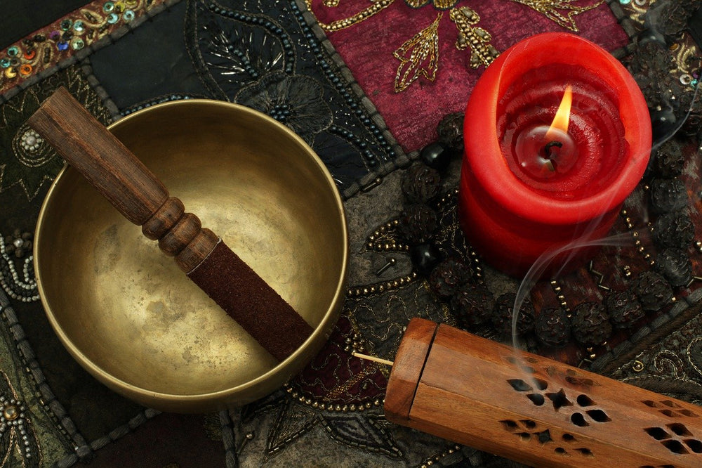 A singing bowl, red candle, and incense holder sit atop an ornate tapestry.