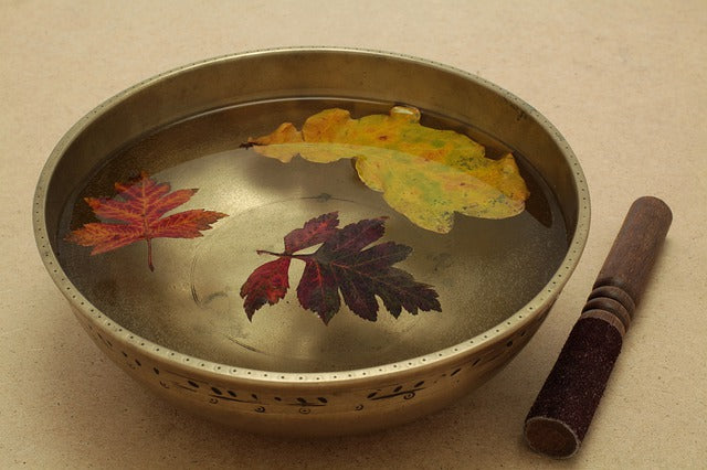 Dried autumn leaves float in singing bowl full of water. 