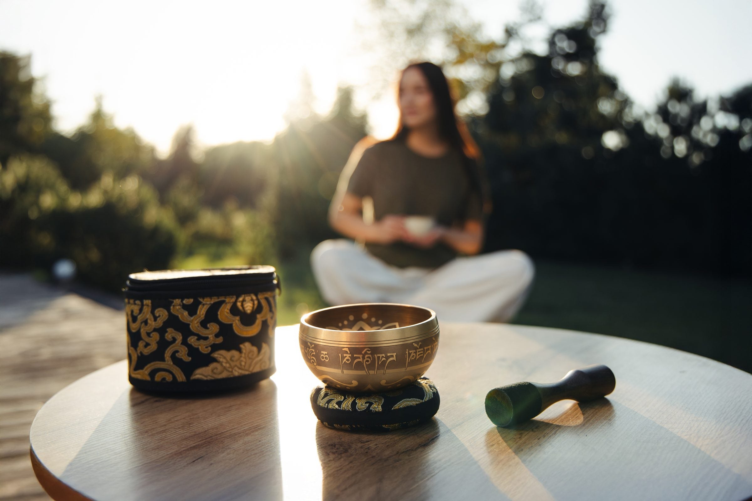 The Golden Harmony singing bowl on its cushion on a garden table in warm evening light