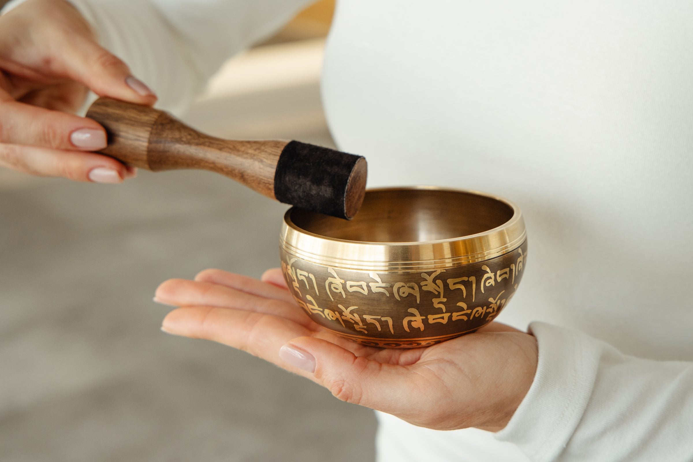 Golden Serenity singing bowl held in the hand, striker ready