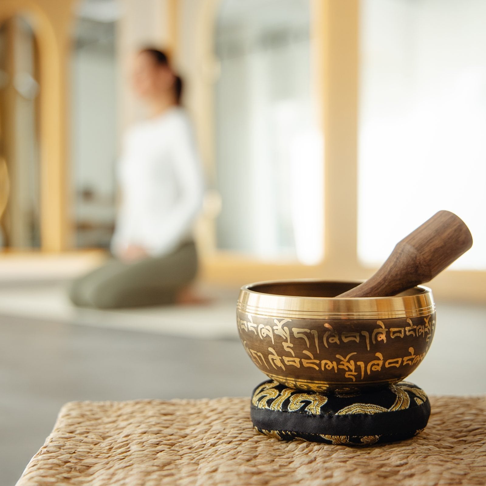 A singing bowl resting on its cushion after playing, with someone sitting quietly behind it