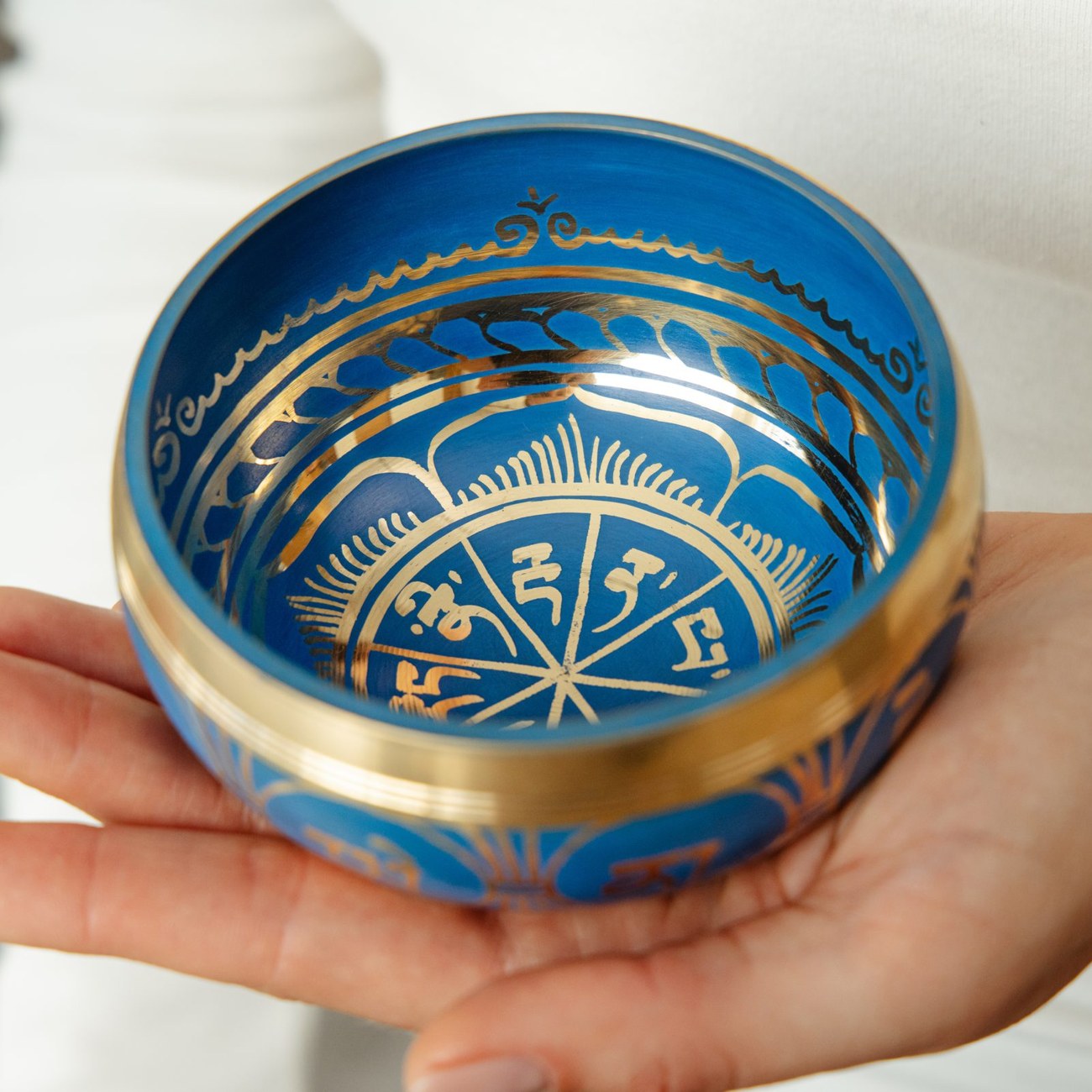 A singing bowl held lightly from underneath on the fingertips as its sound fades