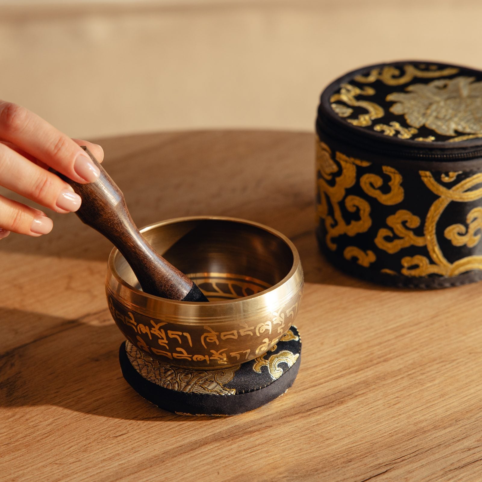 A hand circling the outside of a singing bowl's rim with the wooden side of the striker
