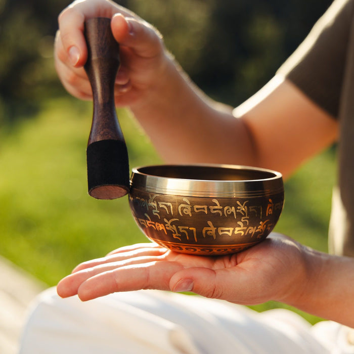 A hand tapping the outside of the bowl with the leather-wrapped end of the striker