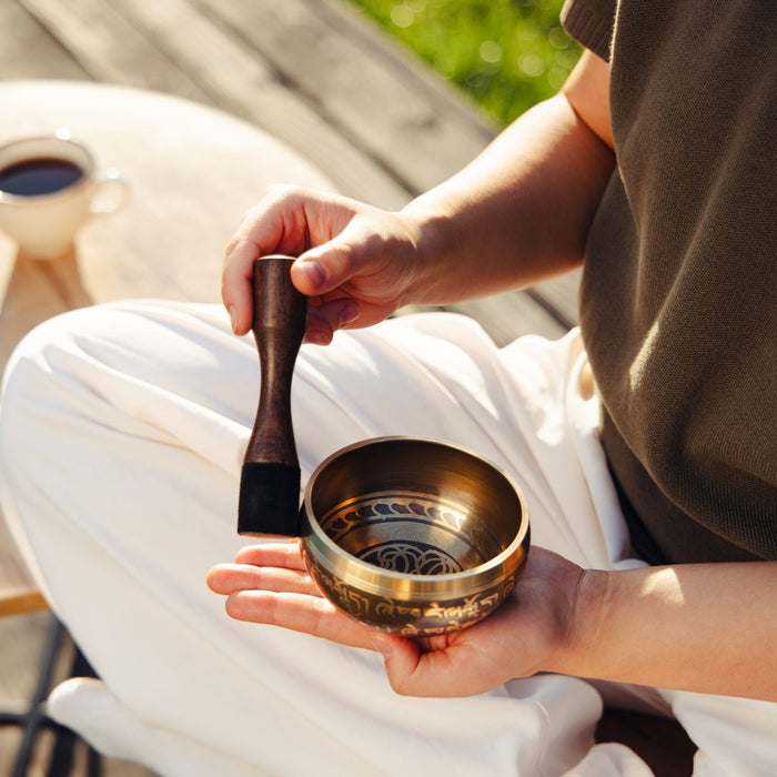 A hand holding a singing bowl, with the striker upright beside the outside of the rim
