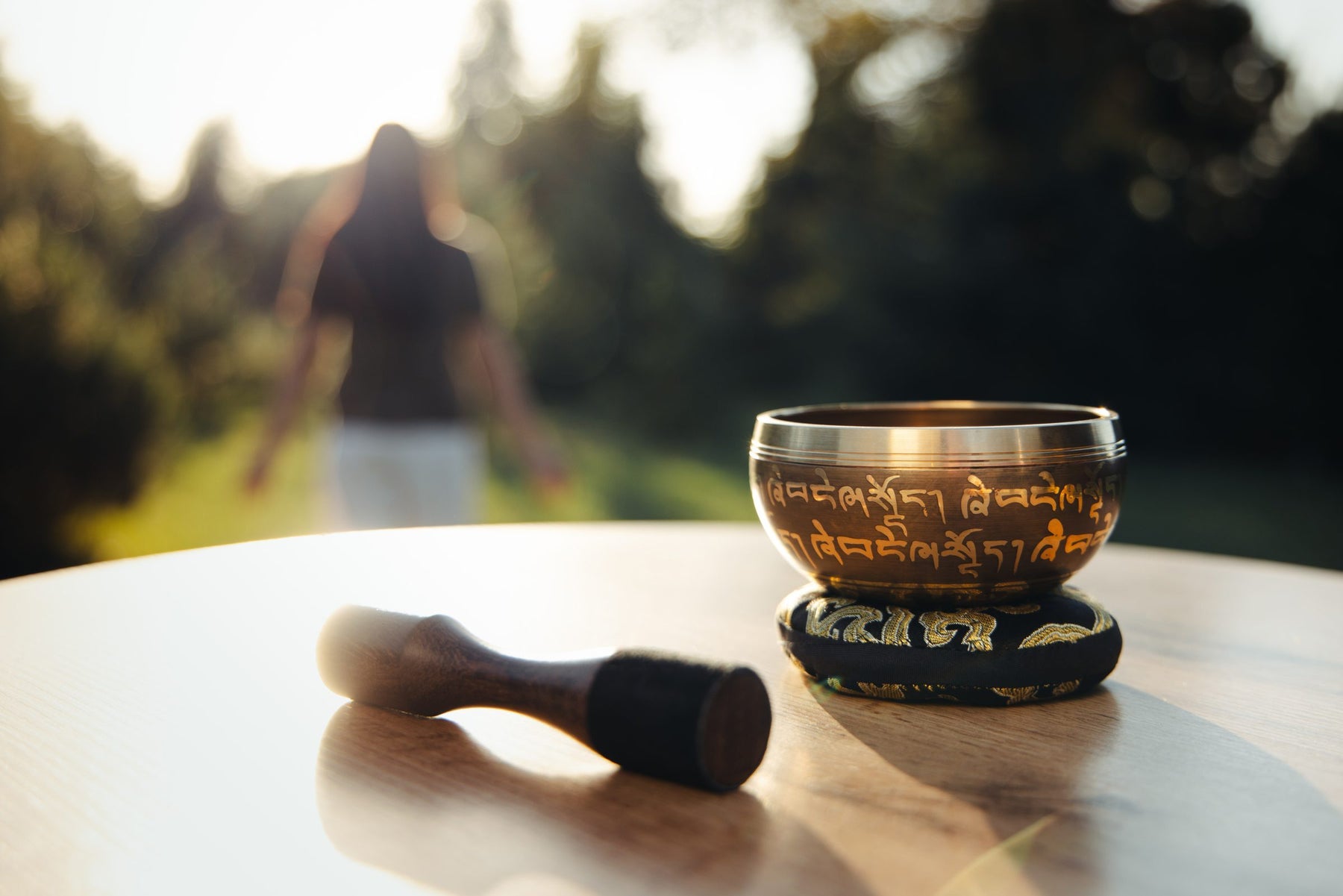 A Silent Mind singing bowl on its cushion, with its striker, on a garden table in warm evening light