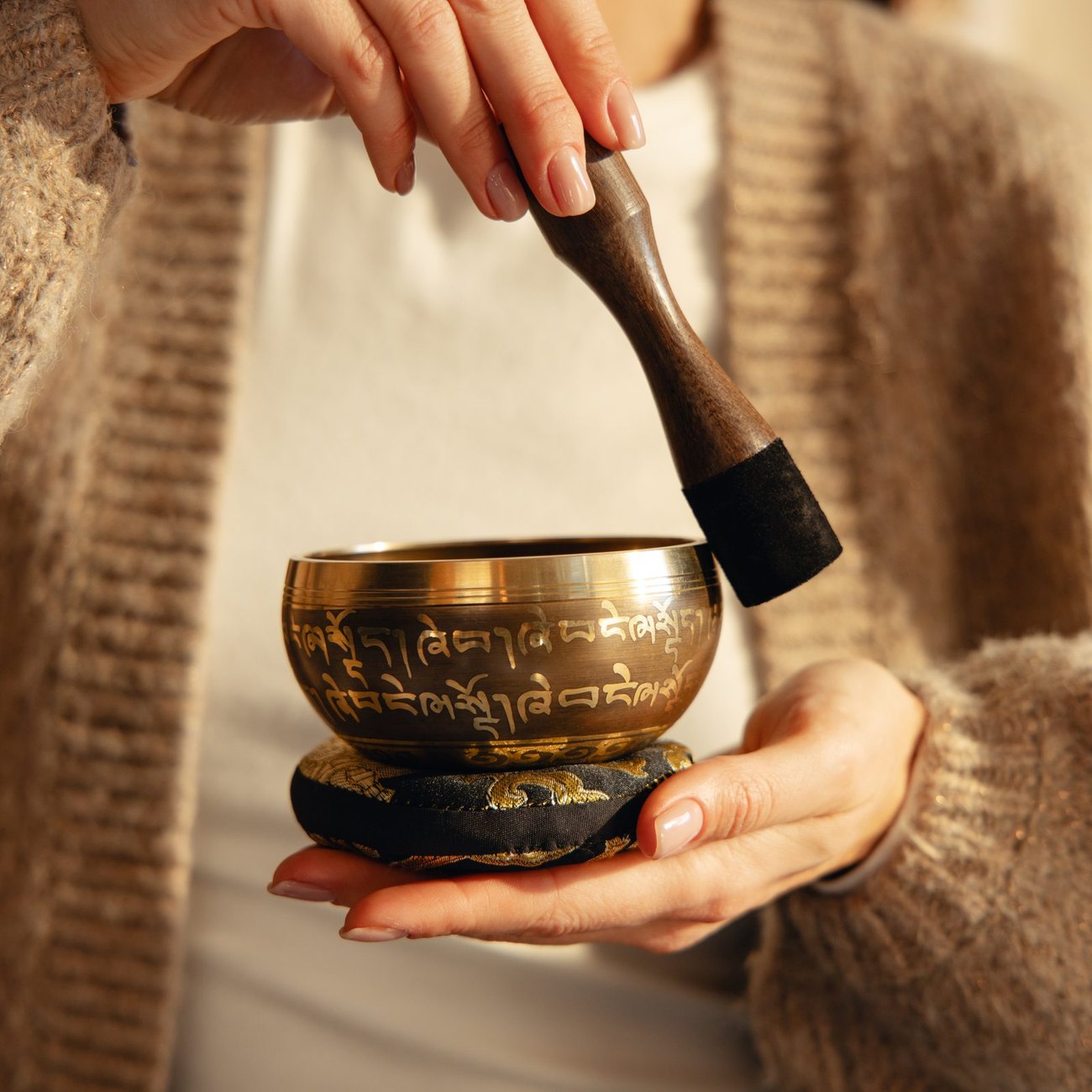 A striker tapping the outside of a singing bowl, just below the rim, with its leather-wrapped end